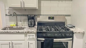 Cozinha com armários brancos, fogão de aço inoxidável, cafeteira e painel de azulejos.