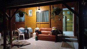 Interior acogedor de una cabaña de madera con un sofá de cuero marrón, una mesa de comedor con sillas y plantas colgantes.