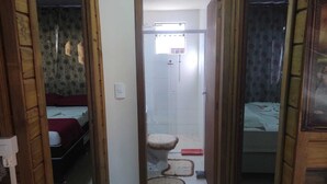 Un pasillo estrecho que lleva a un baño con inodoro, ducha y una cama con una manta roja.