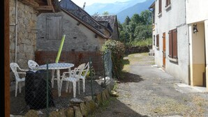 Un stretto vicolo con edifici in pietra, un tavolo e sedie, e montagne sullo sfondo.