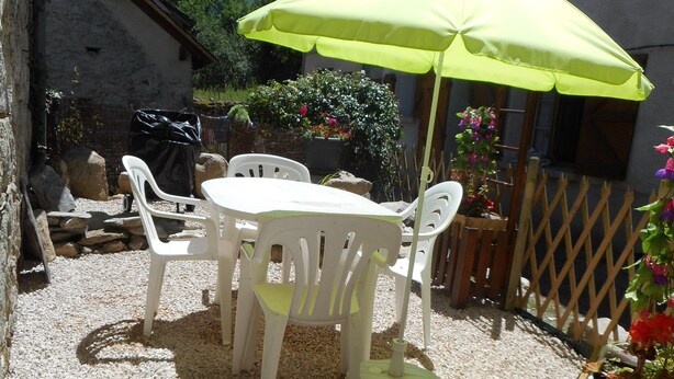 Un'area patio con tavolo e sedie, un ombrellone verde e terreno sterrato.
