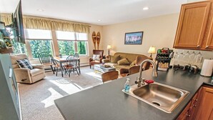 A modern kitchen with a large island, a dining area with a table and chairs, and a living room with a sofa and a coffee table. - Wake Up to Ski Runs, Wind Down by the Fire (Carrabassett Valley)