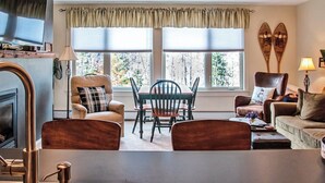 A living room with a dining area, a fireplace, and large windows with curtains. - Wake Up to Ski Runs, Wind Down by the Fire (Carrabassett Valley)