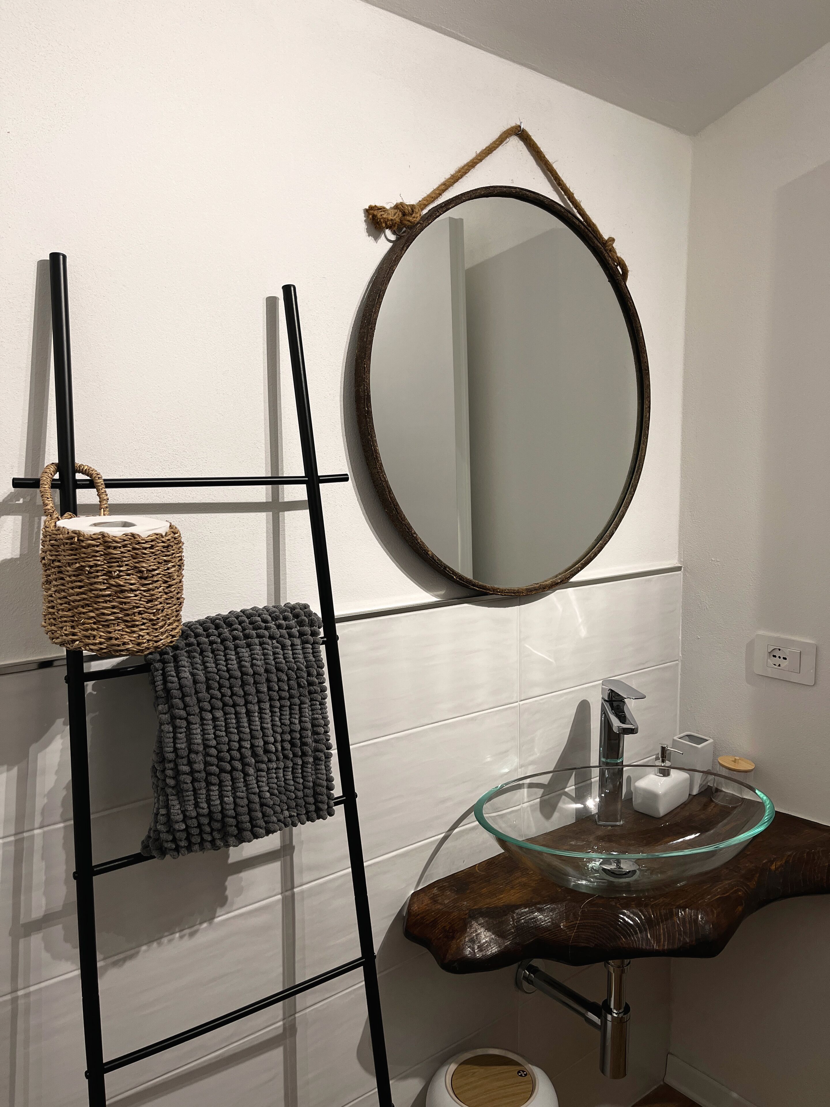A bathroom with a glass sink, a wooden vanity, a black towel rack, and a woven basket.