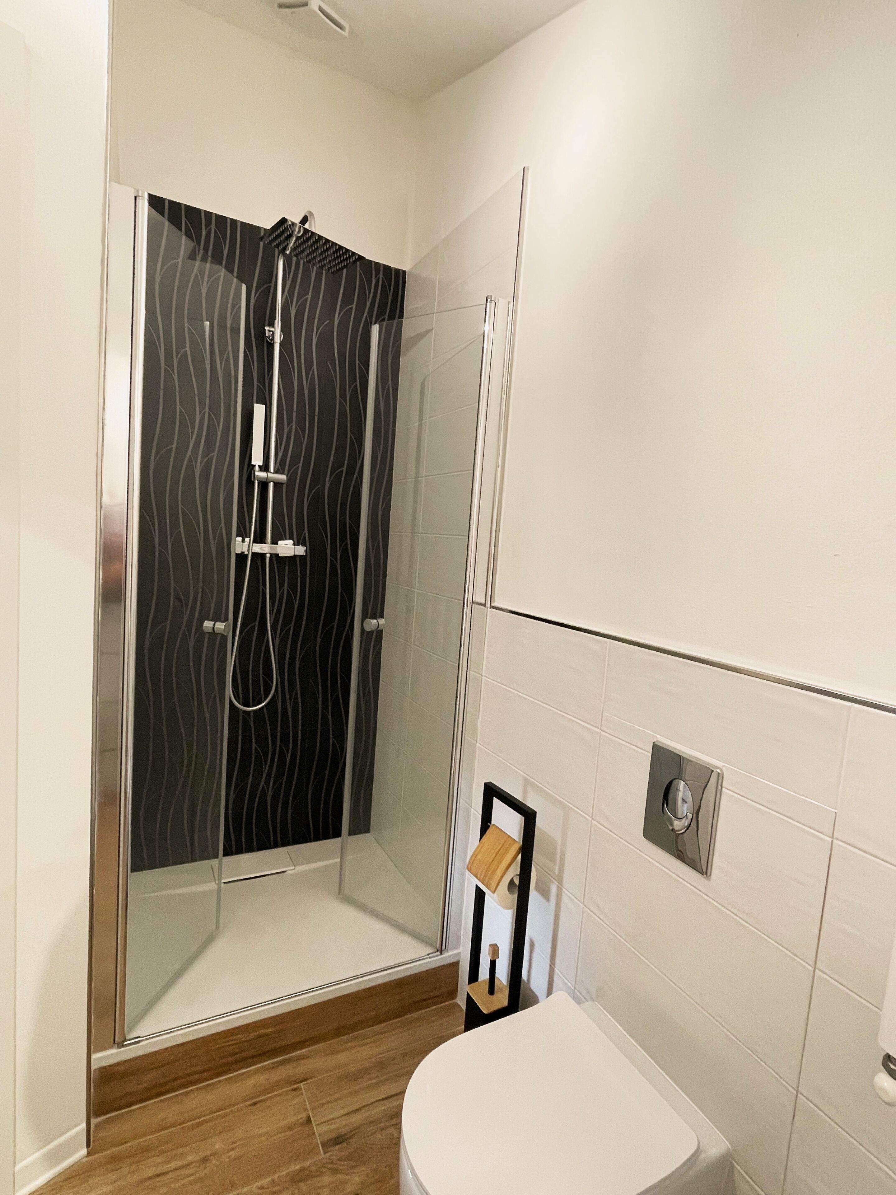 Une salle de bain moderne avec une douche à parois de verre, des toilettes et un plancher en bois.