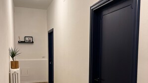 Un couloir avec un plancher en bois, un radiateur, une porte noire et un luminaire au plafond.