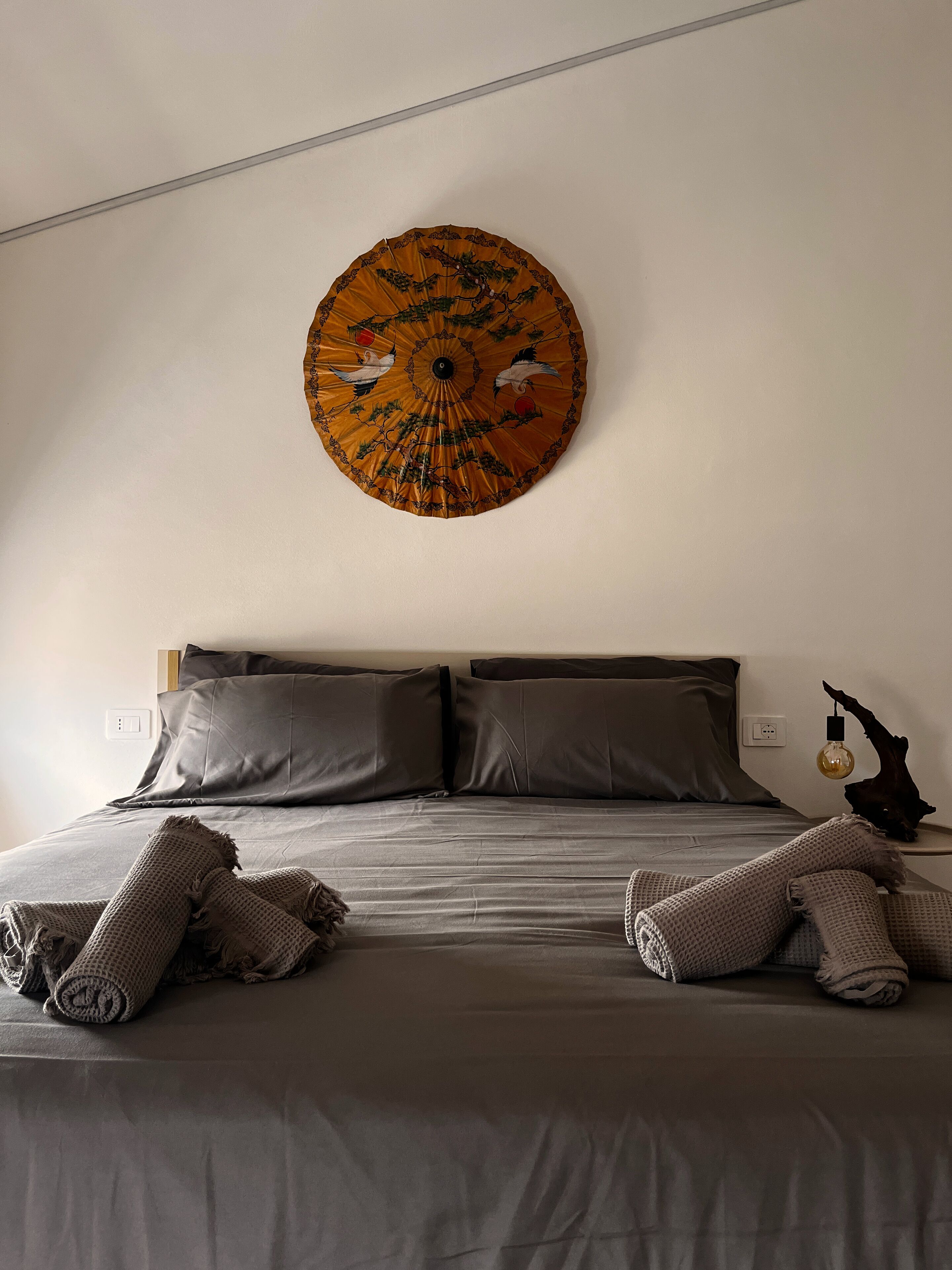 Quarto com cama, almofadas e um objeto decorativo na parede.