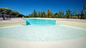 Una piscina cristalina con borde de azulejos, rodeada de follaje y un cielo despejado.