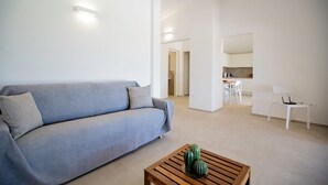 Una sala de estar moderna con un sofá gris, una mesa de centro de madera y una cocina al fondo.