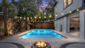 Un jardin avec une piscine, des guirlandes lumineuses et un foyer extérieur.