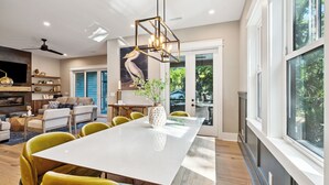 Un vaste salon doté d’une grande table à manger blanche, de chaises jaunes et d’un lustre moderne.
