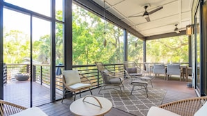 Un espace extérieur abrité, aménagé avec des meubles en osier, une table ronde et offrant une vue sur les arbres à travers de grandes fenêtres.