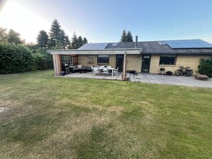 Ein Haus mit Terrasse, Gartenmöbeln, Grill und Solaranlage auf dem Dach.