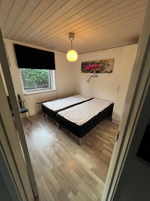 A room with a bed, a window, a chair, and a painting on the wall.