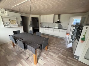 Una cocina moderna con armarios blancos, una mesa de comedor con sillas y un horno empotrado.