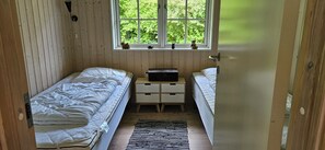A small, wooden-paneled room with two single beds, a nightstand, a window with a view of greenery, and a door.