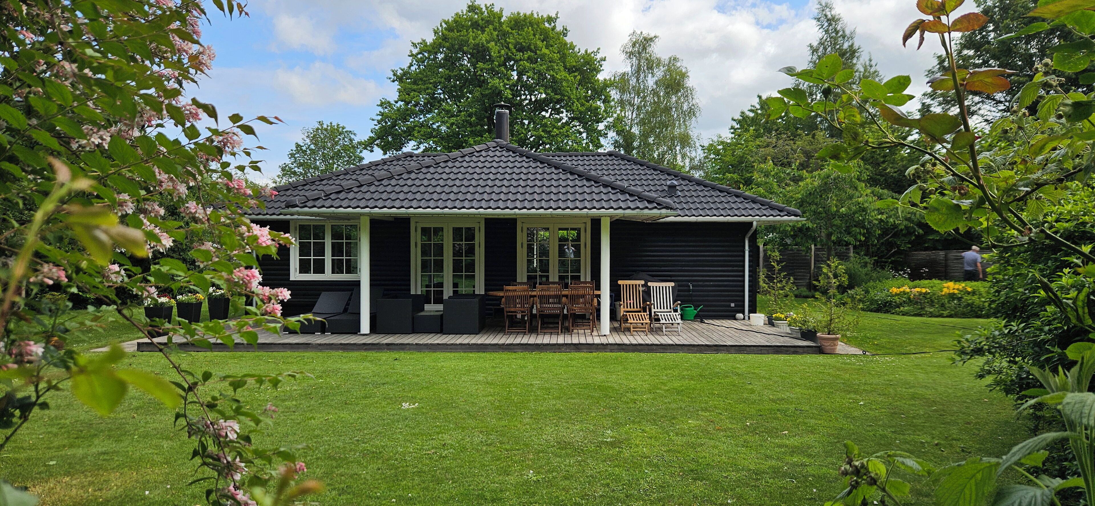 A house with a covered patio, a lawn, and surrounding greenery.