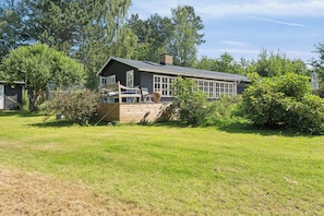 A two-story house with a large deck, surrounded by a grassy yard and trees.
