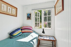 Ein Schlafzimmer mit einem Bett, Kissen, einem Tisch mit Lampe und einem Fenster mit Blick auf Grünflächen.