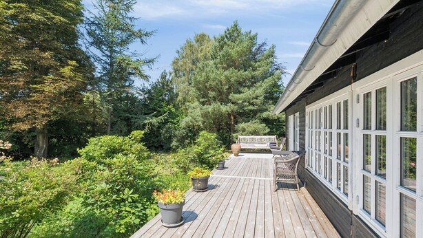 A wooden deck with potted plants, a bench, and a view of trees. - Family-friendly cottage near beach & nature (Vejby)