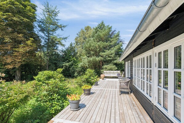 A wooden deck with potted plants, a bench, and a view of trees.