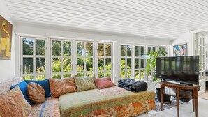 A spacious living room with a large sofa, a television on a stand, and a view through large windows. - Family-friendly cottage near beach & nature (Vejby)