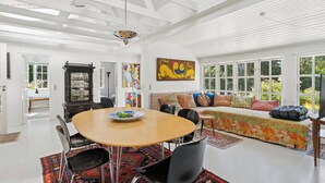 A spacious room with a dining table, chairs, a sofa, and a large window. - Family-friendly cottage near beach & nature (Vejby)