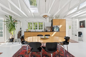 A modern kitchen with white cabinetry, a dining area with a round table and black chairs, and a large potted plant.