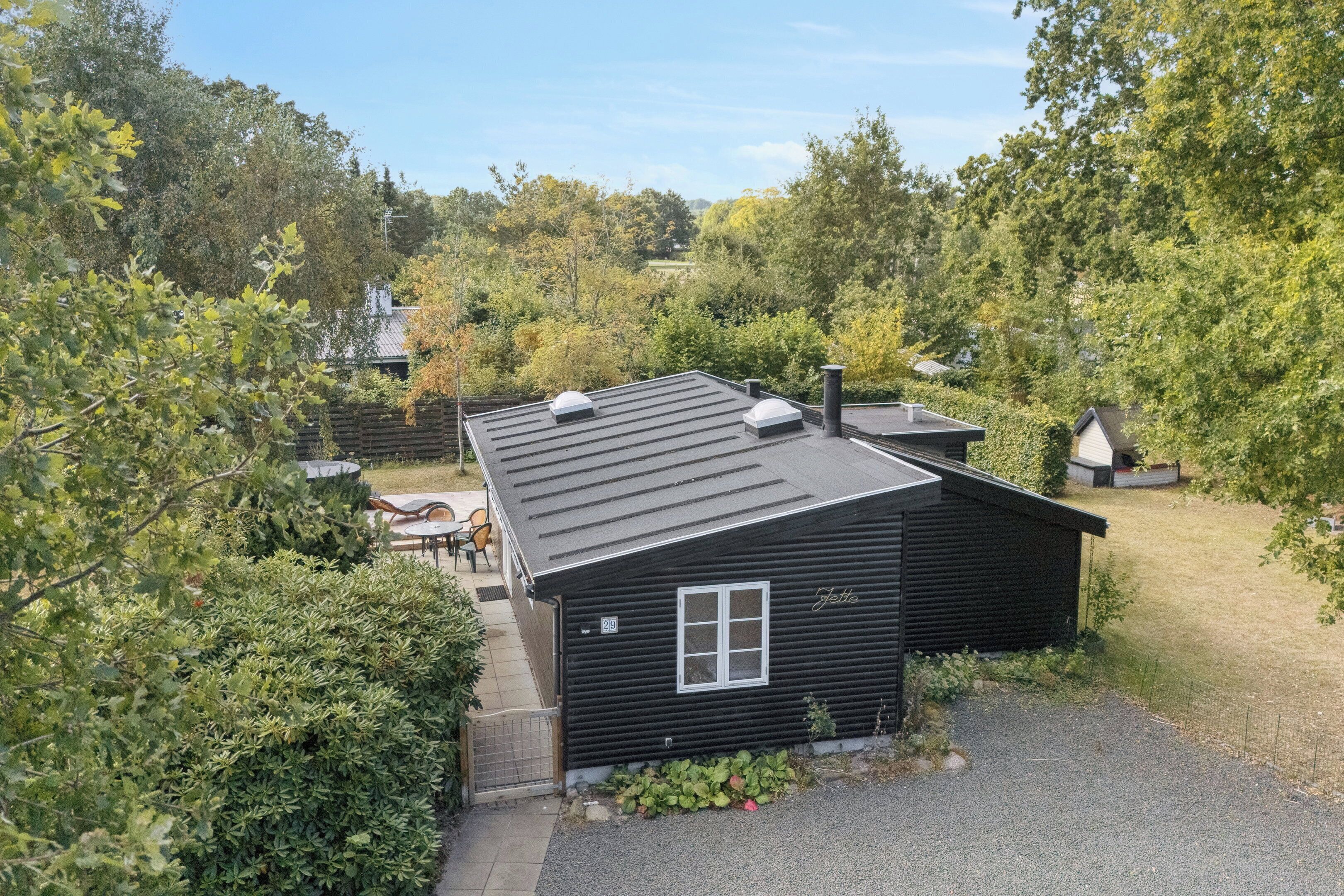 Een zwarte hut met een raam en schoorsteen, omringd door bomen en een heldere lucht.