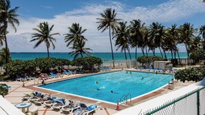 A swimming pool with lounge chairs and palm trees, surrounded by a fence.