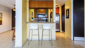 Una cocina compacta con una isla central, dos taburetes de bar, armarios de madera, un microondas y un refrigerador.