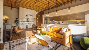 A modern living room with a wooden ceiling, a sofa, a coffee table, and a kitchen area in the background. - Historic Elegance with Balcony Downtown View (Ogden)