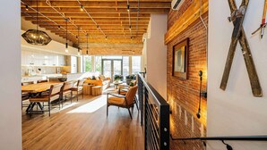 A spacious dining area with wooden flooring and modern furniture, a kitchen with white cabinets, and a brick wall with ski equipment. - Historic Elegance with Balcony Downtown View (Ogden)