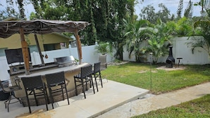 Un espace barbecue extérieur équipé d’un gril, de chaises et d’un coin salon abrité.