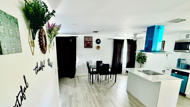 A modern kitchen with a white island, a dining area with a black table and chairs, and a living space with a black curtain. - Serene 3-bedroom house with AC in Fort Lauderdale (Fort Lauderdale)