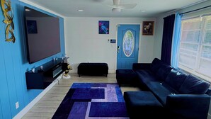 A modern living room with a large flat-screen TV, a black sofa, a coffee table, and a decorative wall piece. - Serene 3-bedroom house with AC in Fort Lauderdale (Fort Lauderdale)