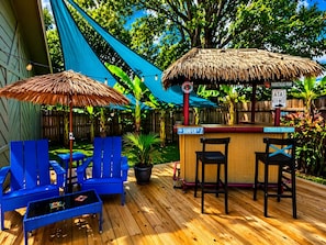 A wooden deck with blue chairs, a thatched-roof bar, and a sign for Surfer St.
