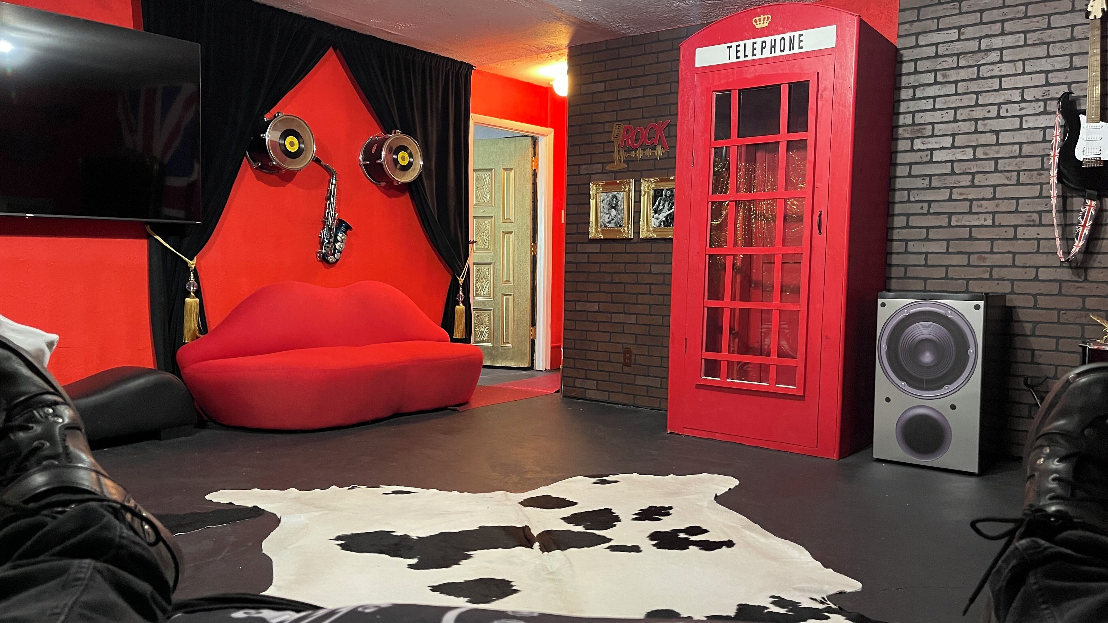 Ein Zimmer mit einer roten Telefonzelle, einem roten Sofa, einem Kuhfellteppich und einem Lautsprecher.