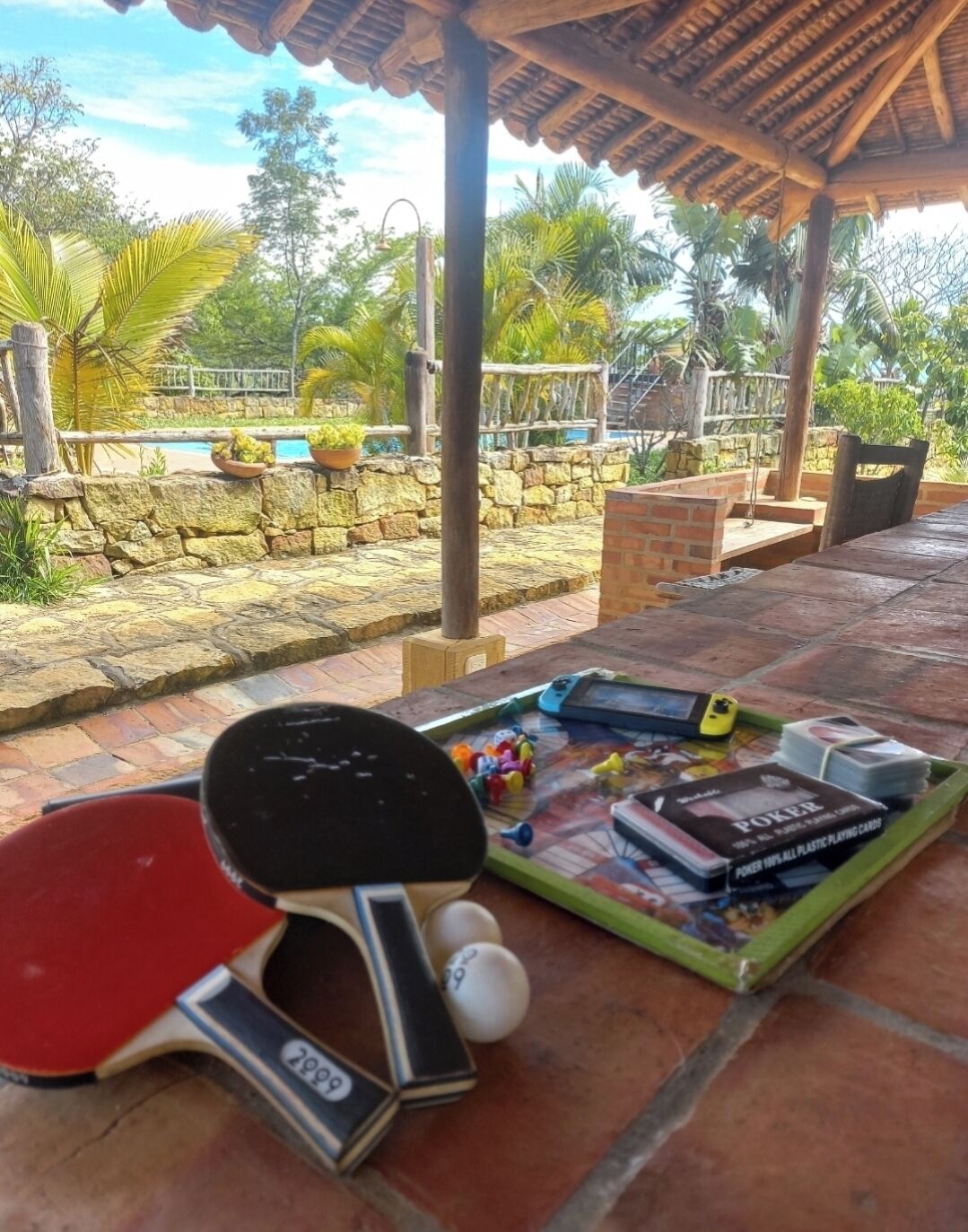 Uma mesa com uma raquete de pingue-pongue, um smartphone e um tabuleiro com cartas e uma garrafa.