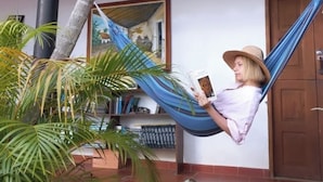 A person relaxing in a hammock, reading a book, with a bookshelf and a door in the background. - San Rafael del Campo Barichara (Barichara)