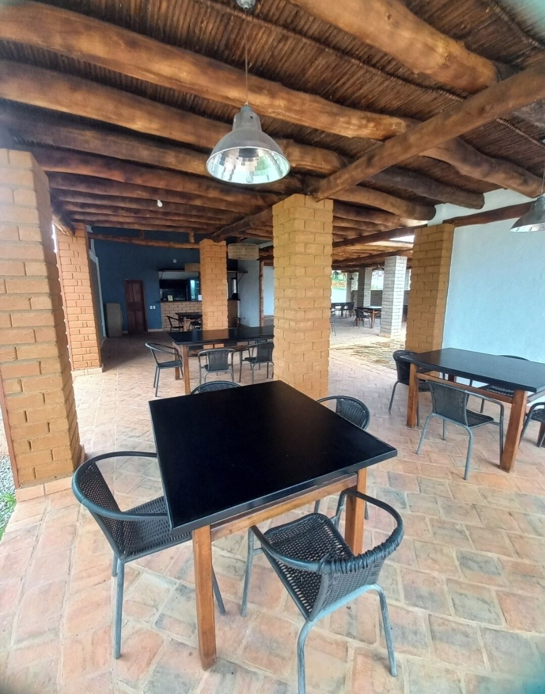 Un patio al aire libre con muros de ladrillo, vigas de madera y mesas y sillas de metal.