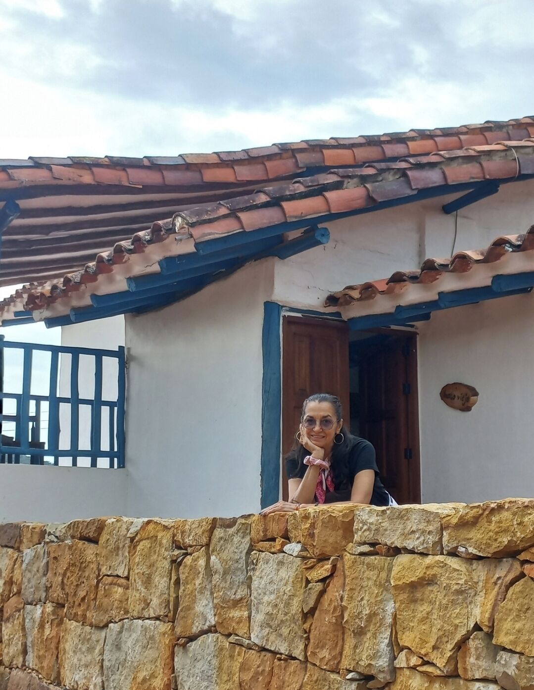 A person leaning on a stone wall outside a building with a tiled roof and a wooden door.