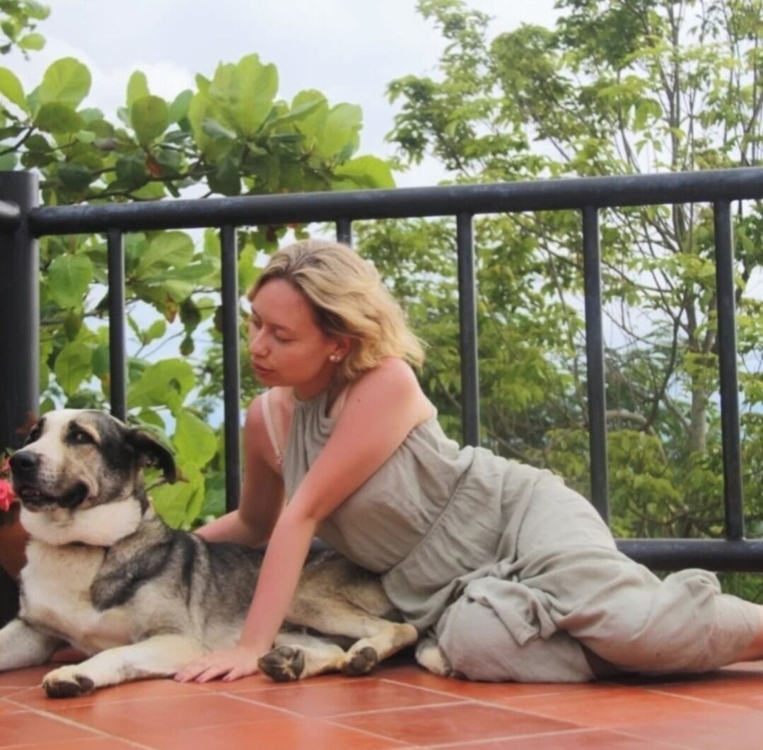 Een persoon zit op een betegelde vloer buiten, leunt tegen een reling, met een hond ernaast.