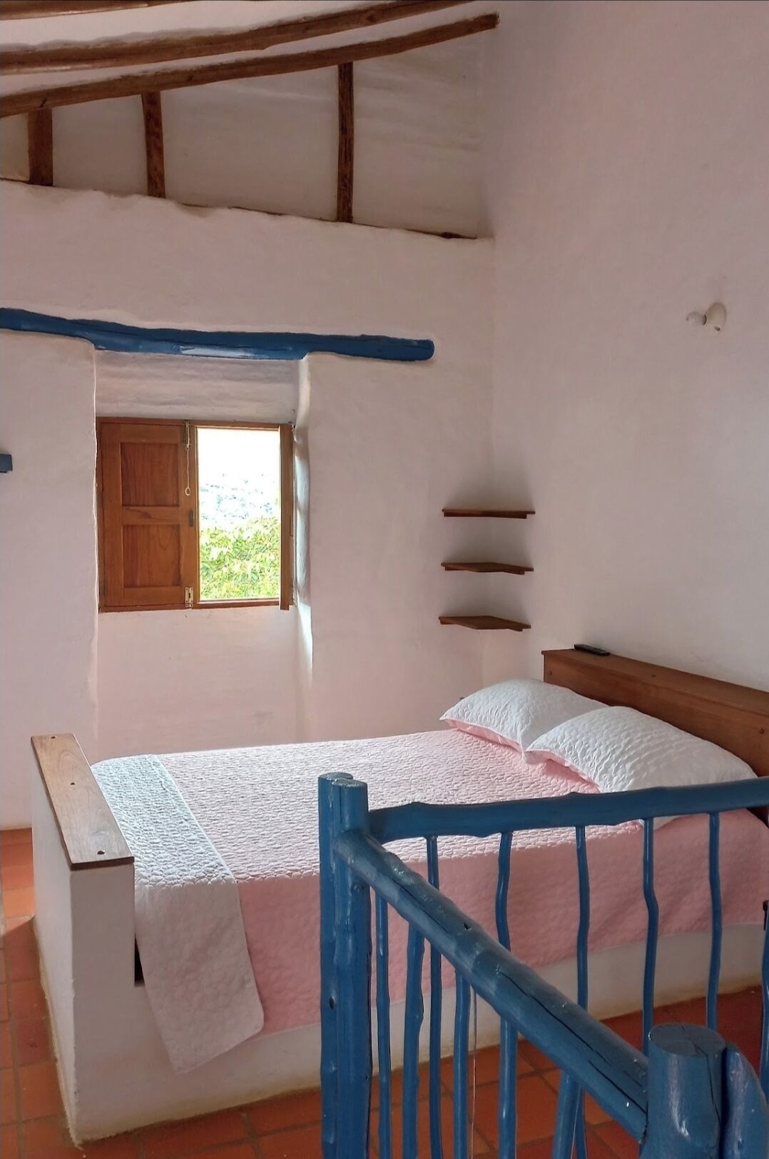 Quarto rústico com cama de madeira, uma pequena janela e teto inclinado.