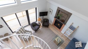 A spacious living room with a fireplace, a staircase, and large windows.
