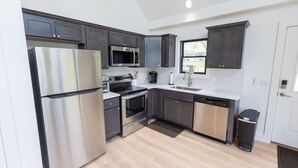 A modern kitchen with stainless steel appliances, dark cabinetry, and a large window providing natural light.