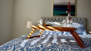 A bedroom with a bed, a bedside table, a lamp, a cup, a bowl, and a framed picture on the wall.