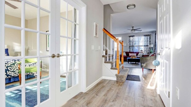 A spacious hallway with a wooden floor, white-framed glass doors leading to a living area with a sofa and a coffee table.