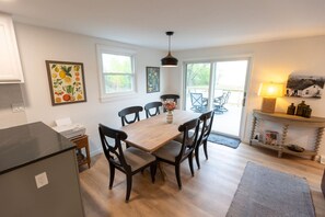 Een moderne keuken met een houten eettafel, zwarte stoelen en een hanglamp. Er zijn twee ramen en een uitzicht op de omgeving.