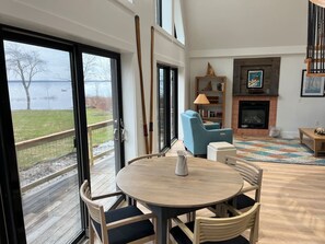 Amplia sala de estar con chimenea, una mesa redonda de madera y vistas a un lago a través de amplios ventanales.
